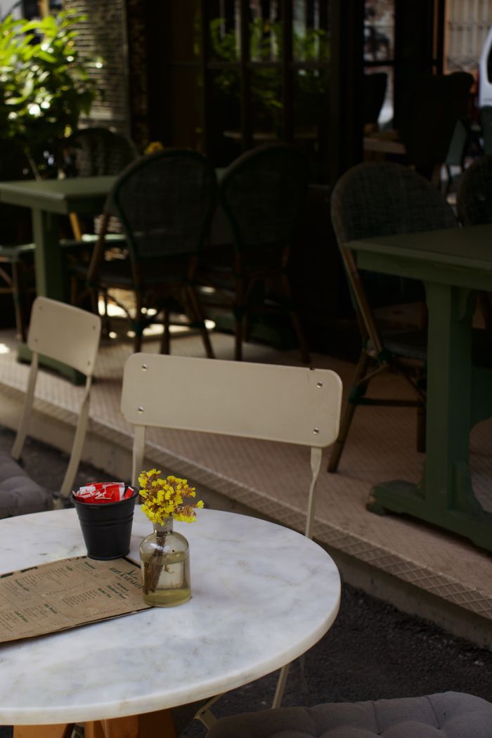 collection-02 Cozy sidewalk cafe with tables, chairs, and yellow flowers in a vase for a serene dining experience.